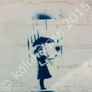 Blaues Graffiti auf weißer Fassade: eine Frau steht unter einem Regenschirm und streckt einem Herz ihre Hand entgegen